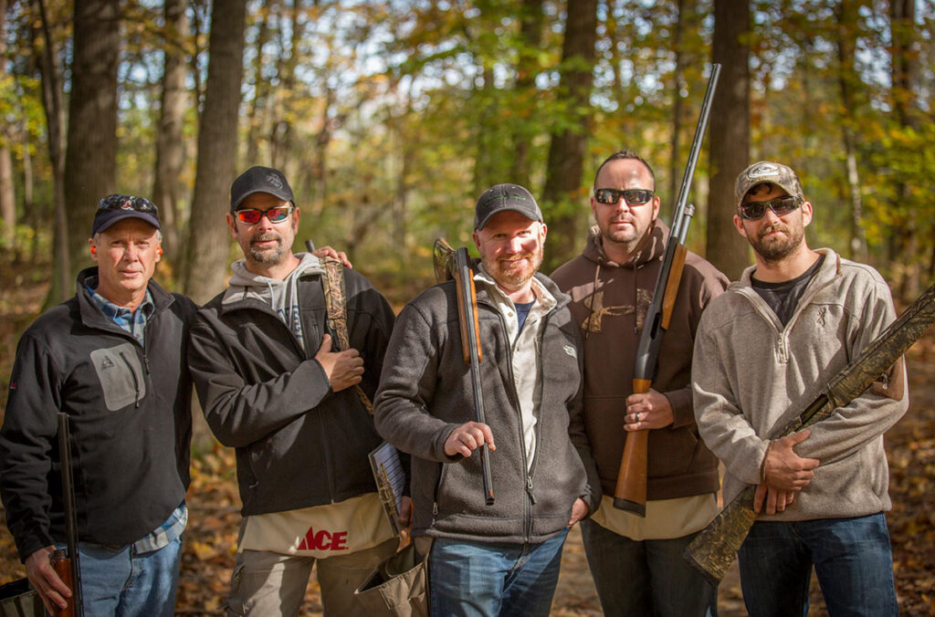five men stand in the woods holding guns