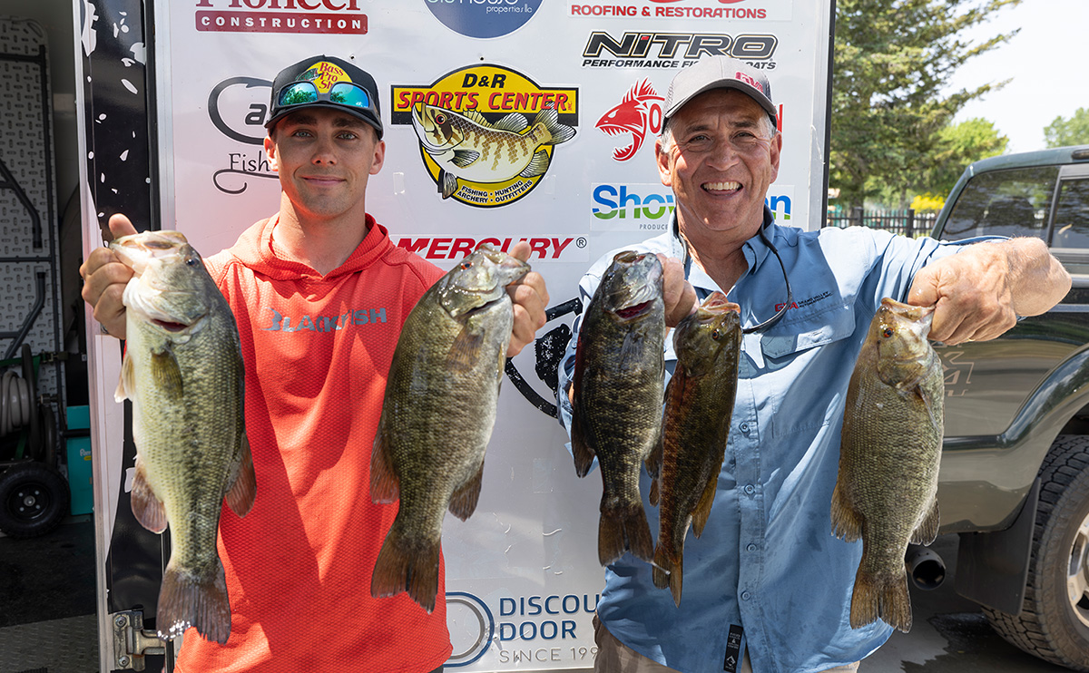 two men hold up fish they caught in front of a banner with logos