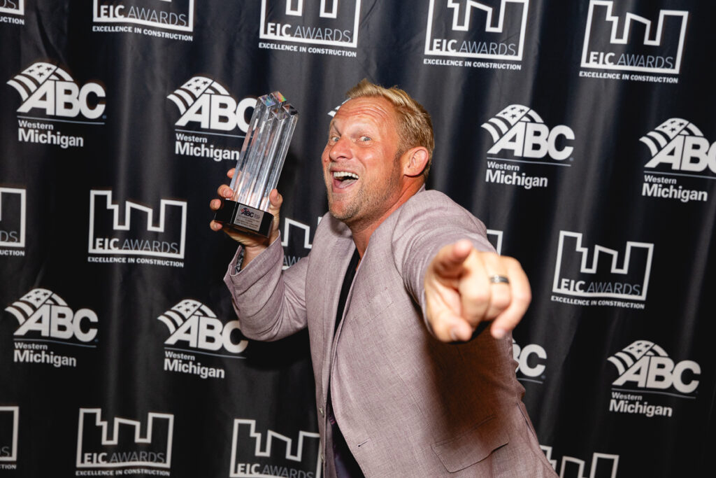 An ABC West Michigan EIC award winner eccentrically pointing towards the camera and hold their award